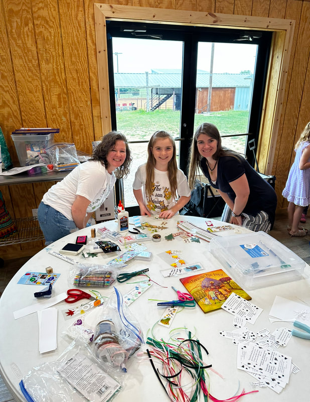 Two volunteers and a student at a craft table full of supplies at the co-op