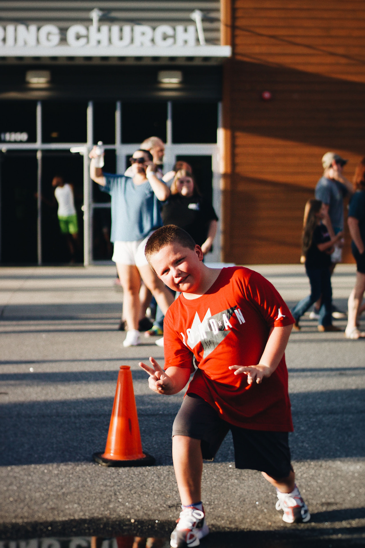A grinning boy throwing a peace sign outside a church building