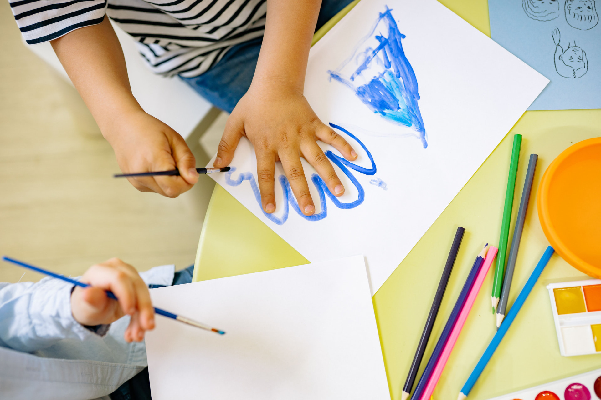 Overhead view of two children painting with watercolors at a table