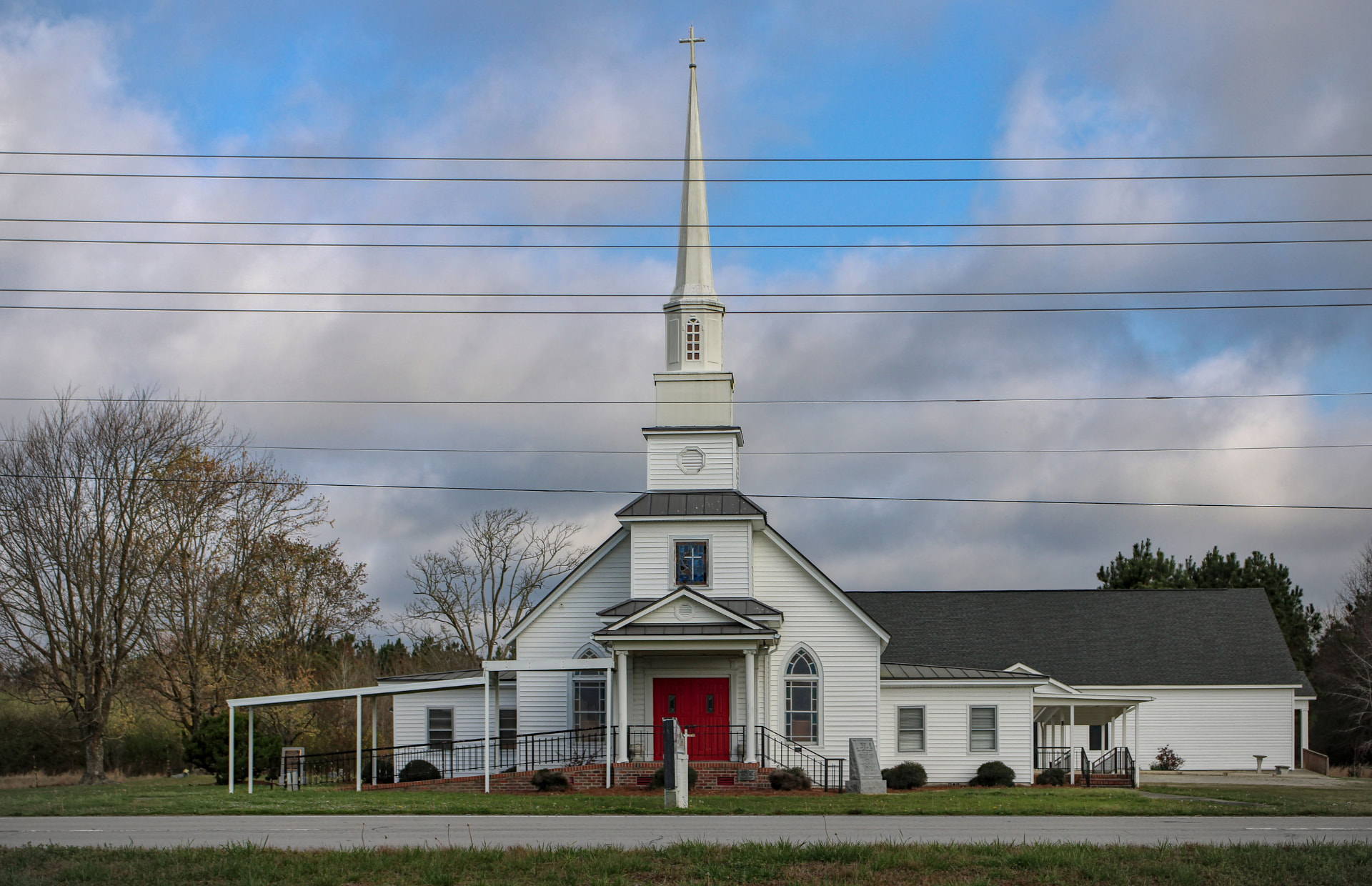 A small white country church with a tall steeple beside a rural road