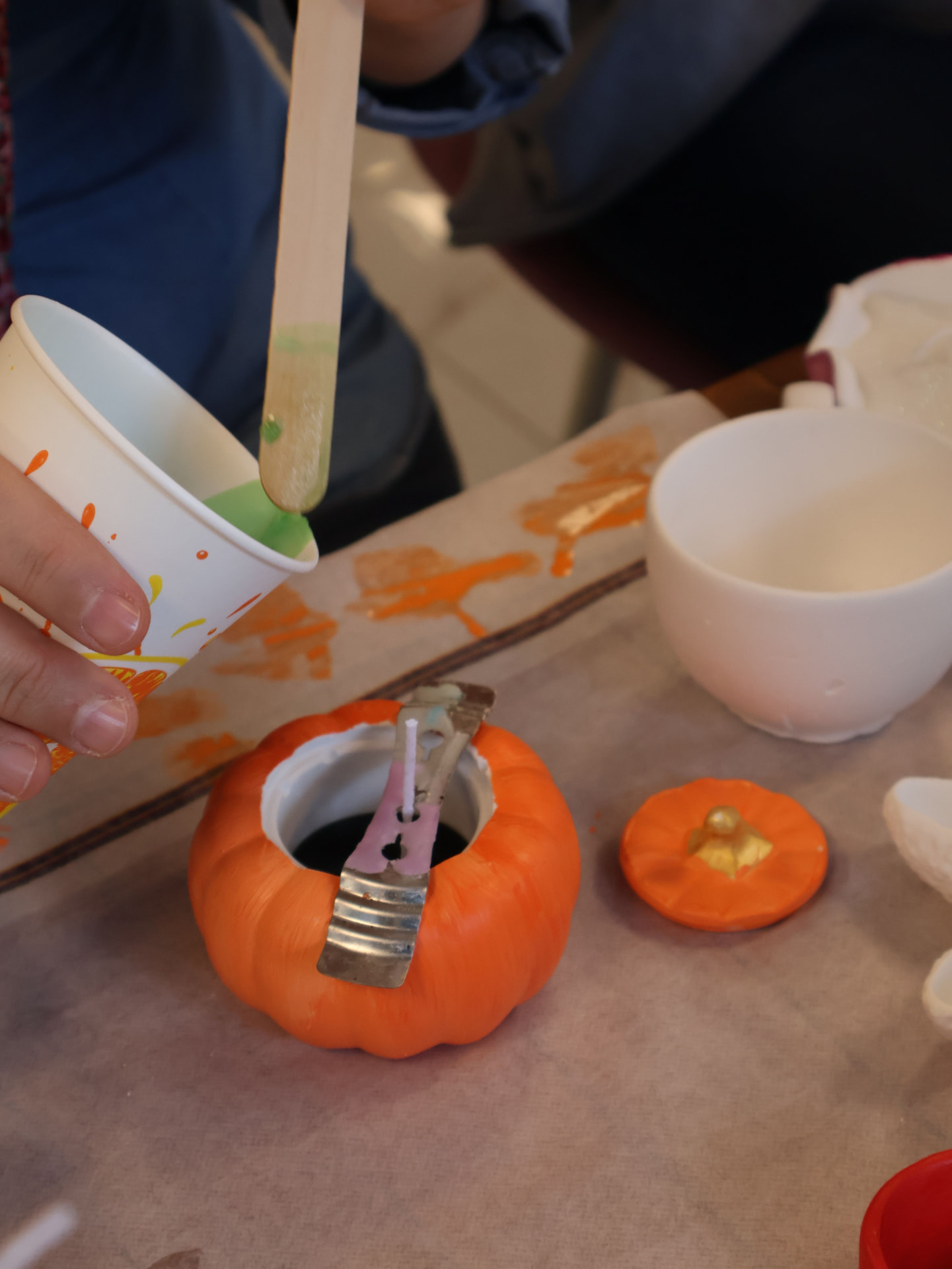 A child painting a small ceramic pumpkin at a craft table
