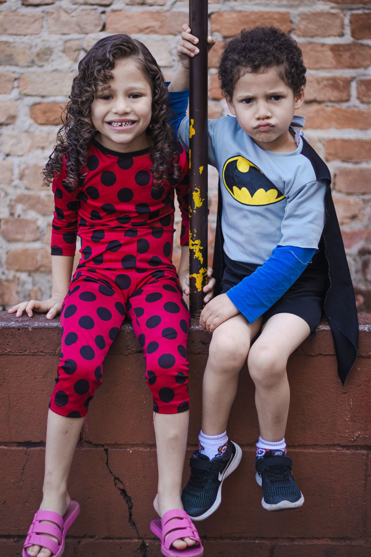 Two kids in superhero costumes sitting together on a ledge